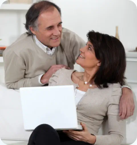 A middle-aged couple are looking at a laptop together in their living room