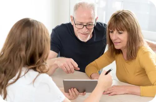 A middle aged couple is being shown information on a tablet by a staff member