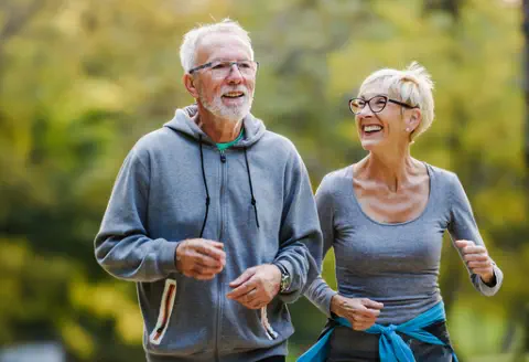 A middle-aged couple in activewear is walking briskly outside